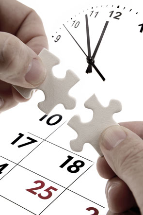 Hands holding two matching jigsaw pieces in front of a clock and a calendar.